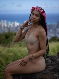 a woman in a bikini sitting on top of a rock