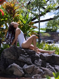 a woman in a white bathing suit sitting on a rock